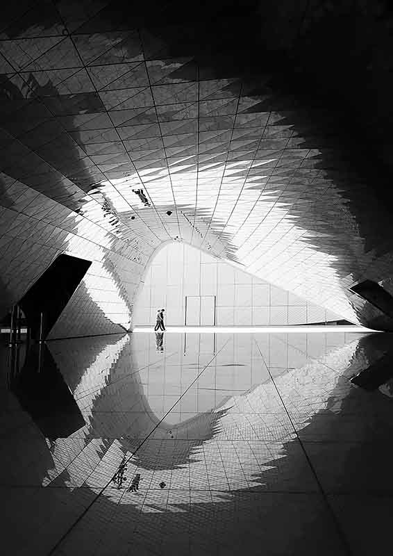 Carbon Tunnel Vision - B&W photo of tiled tunnel with mirrored floor and two distant figures crossing in the distance