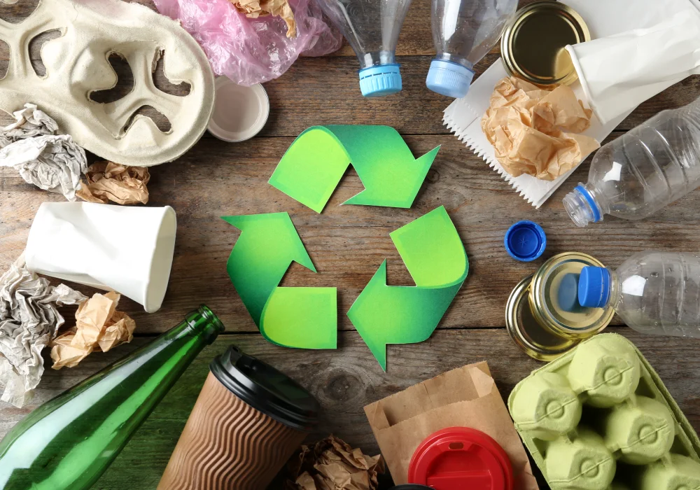 The recycling symbol in green, surrounded by recyclable waste on a tabletop.