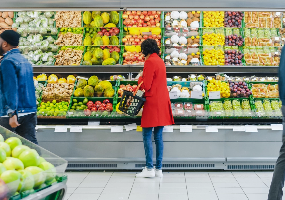 A woman in a red jacket browses fruit and veg in a supermarket.